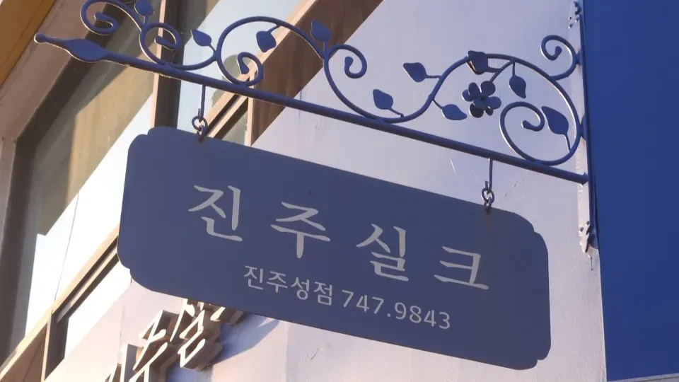 파란 철제 넝쿨 장식 아래 걸린 진주실크 진주성점 간판. ‘진주실크 진주성점 747.9843’이라고 적혀 있다
